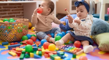 Two toddlers playing with balls and xylophone sitting on floor at kindergarten